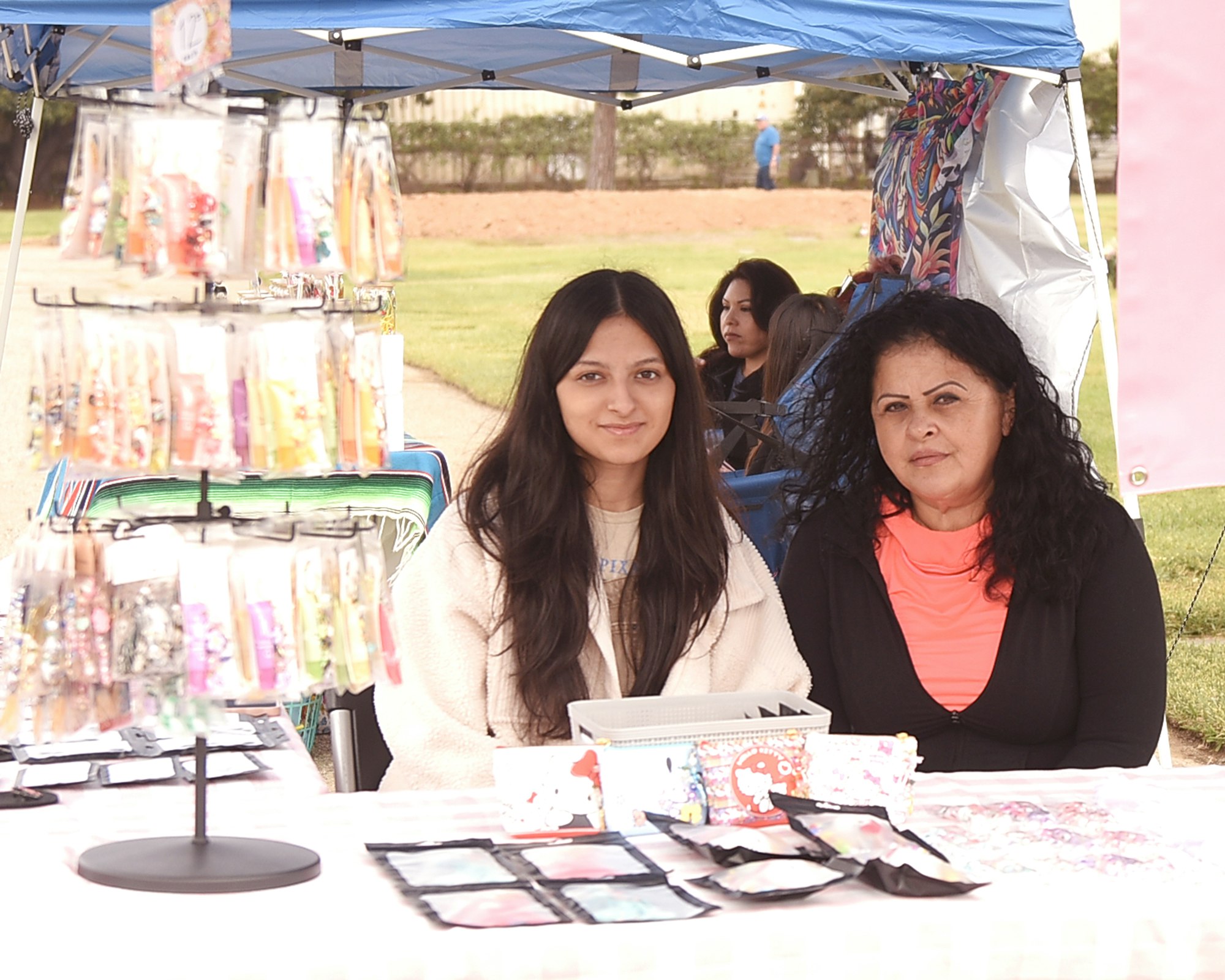 Two people at a stall with jewelry and colorful items, possibly at a market or fair.