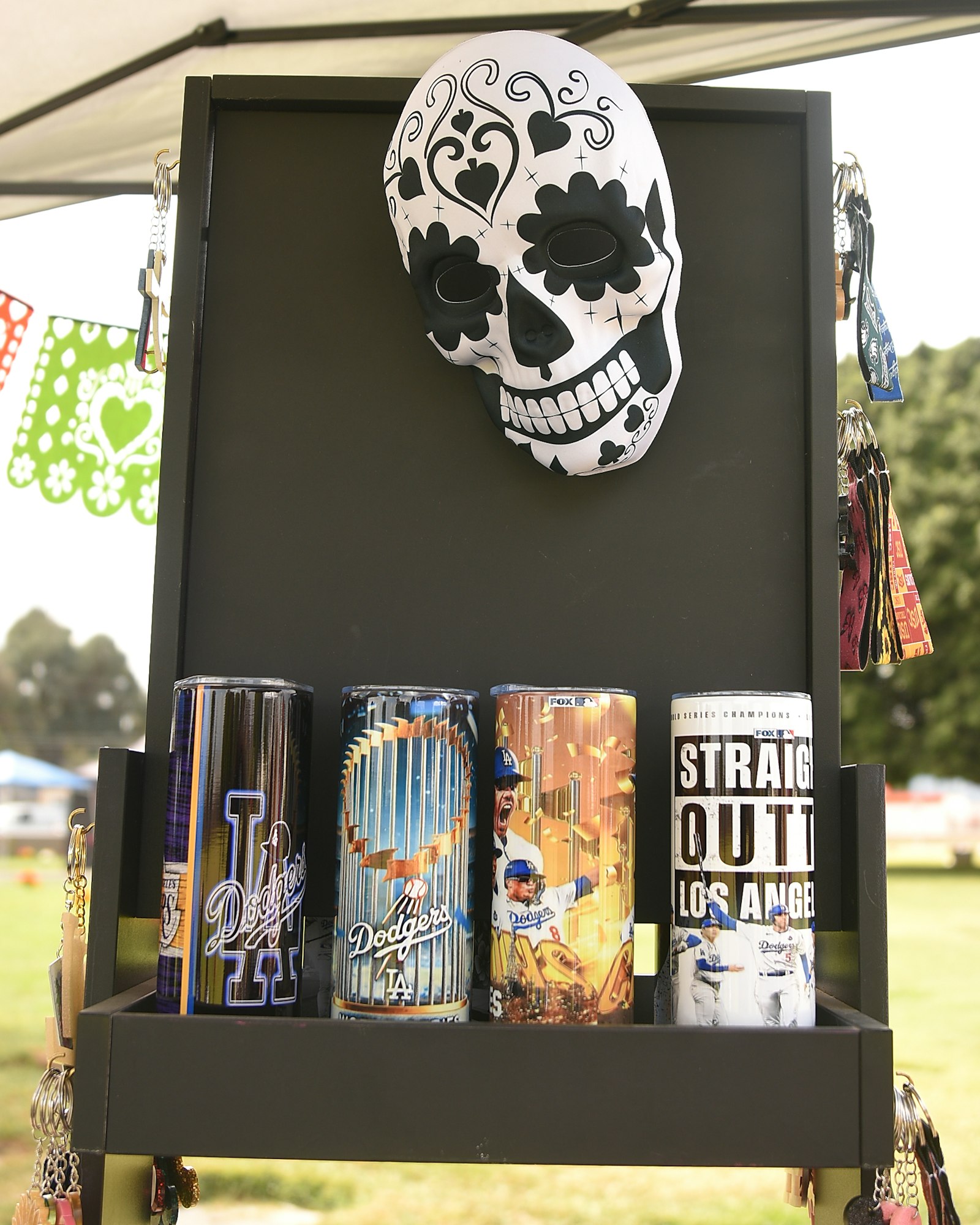 Decorative skull mask with LA Dodgers-themed cans and keychains displayed on a black shelf.