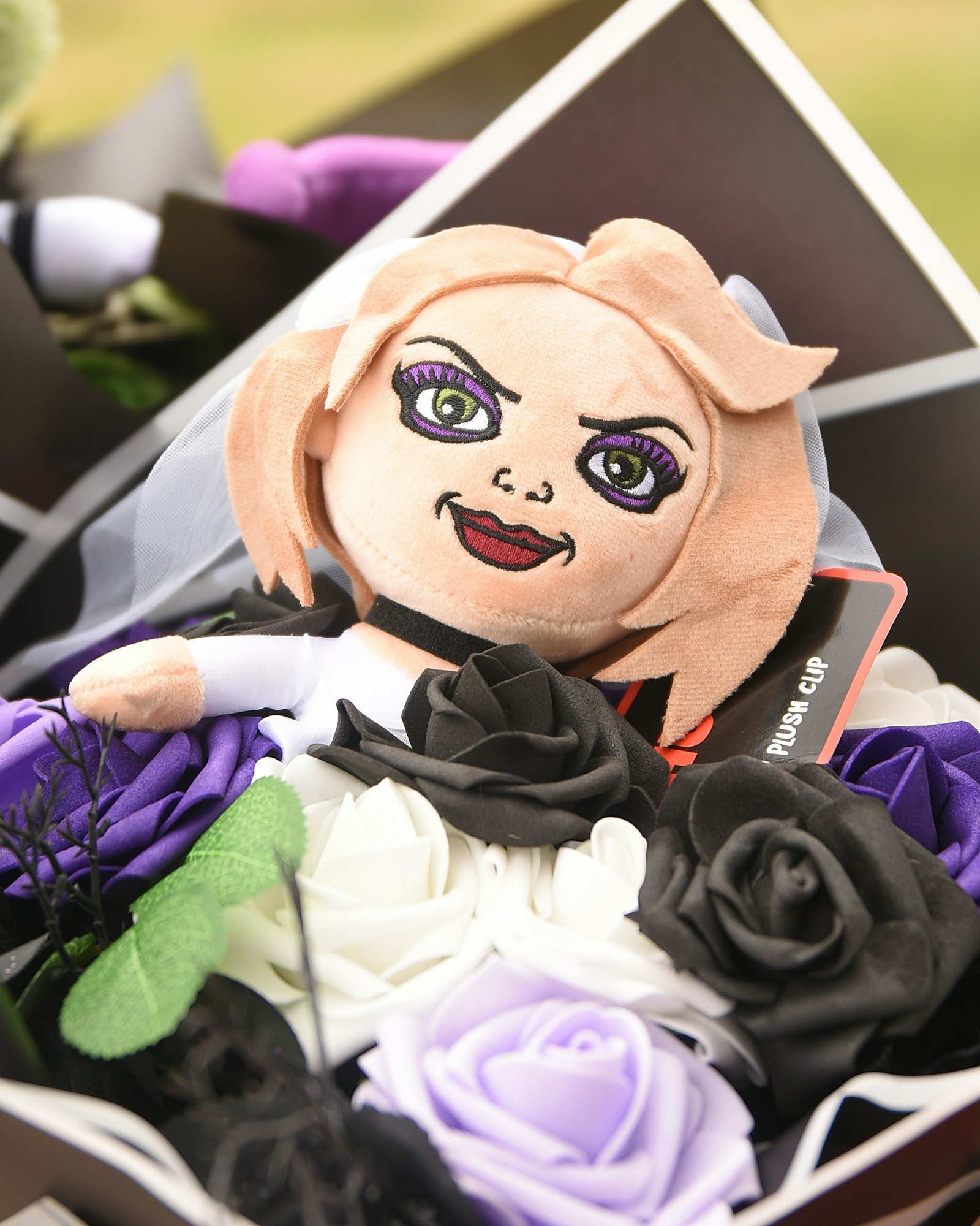 A plush toy with cartoonish features surrounded by artificial purple and black roses, presented like a bouquet.