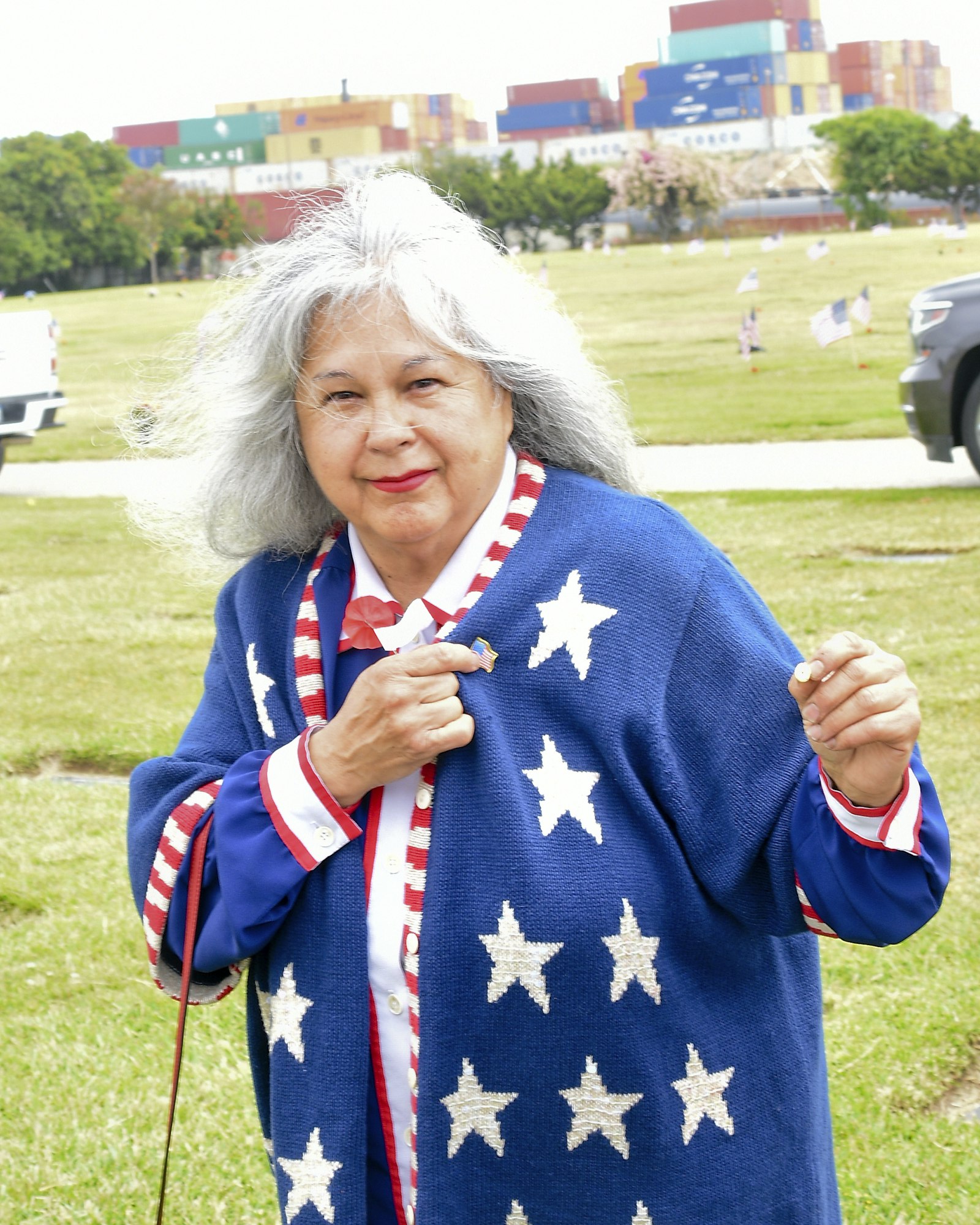 A person wearing a star-patterned shawl and patriotic colors standing outdoors with containers in the background.