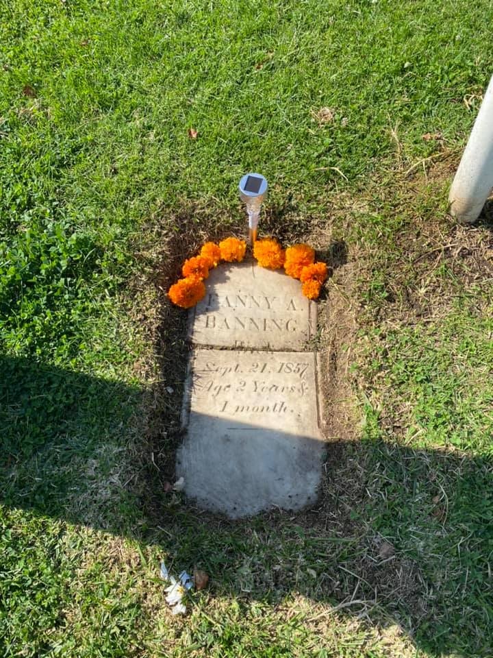The image shows a grave marked for Fanny A. Danning, born September 21, 1857, passed at age 2 years and 1 month, decorated with marigolds.