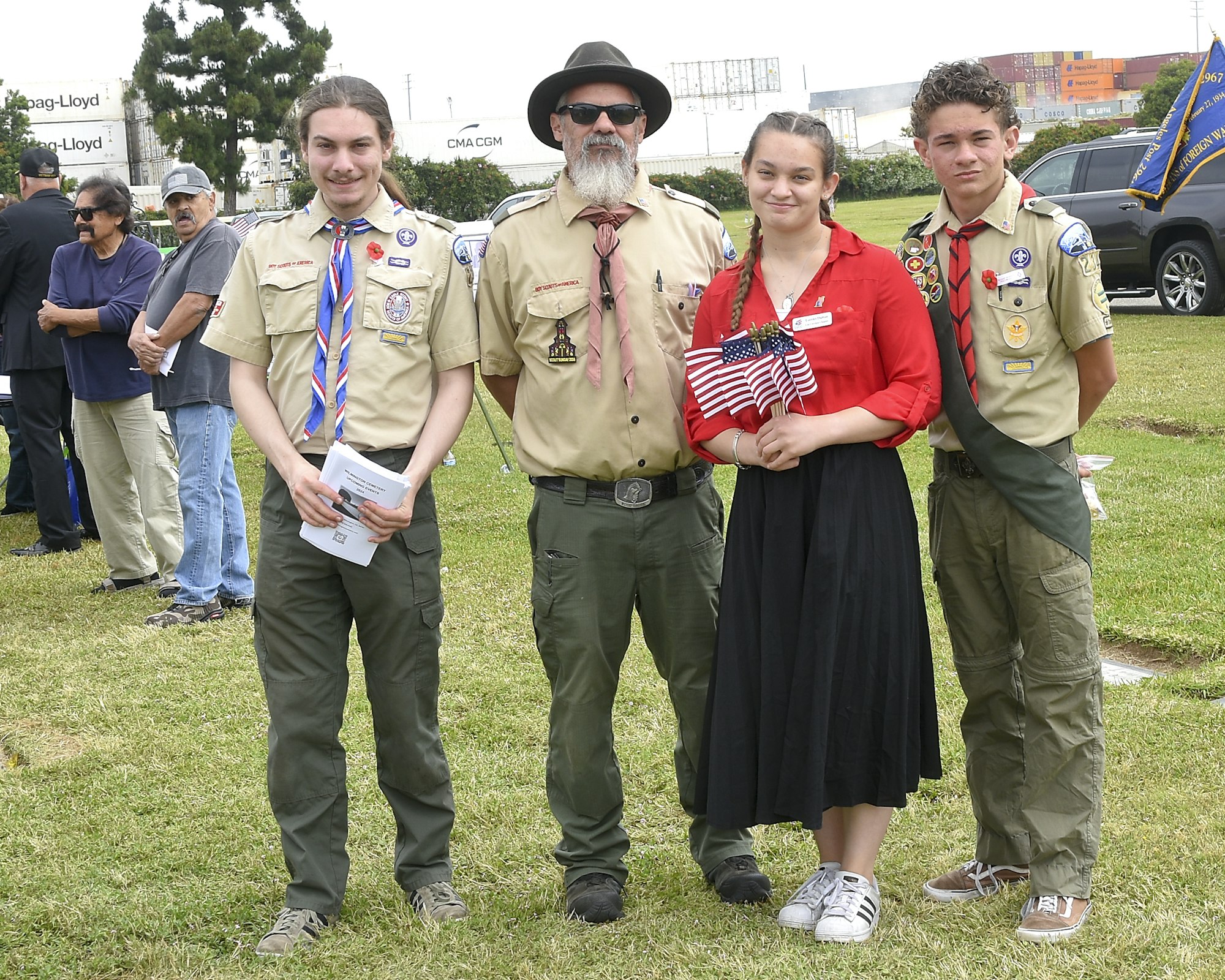 Three scouts and an adult leader pose together outdoors, with American flags held by one individual.