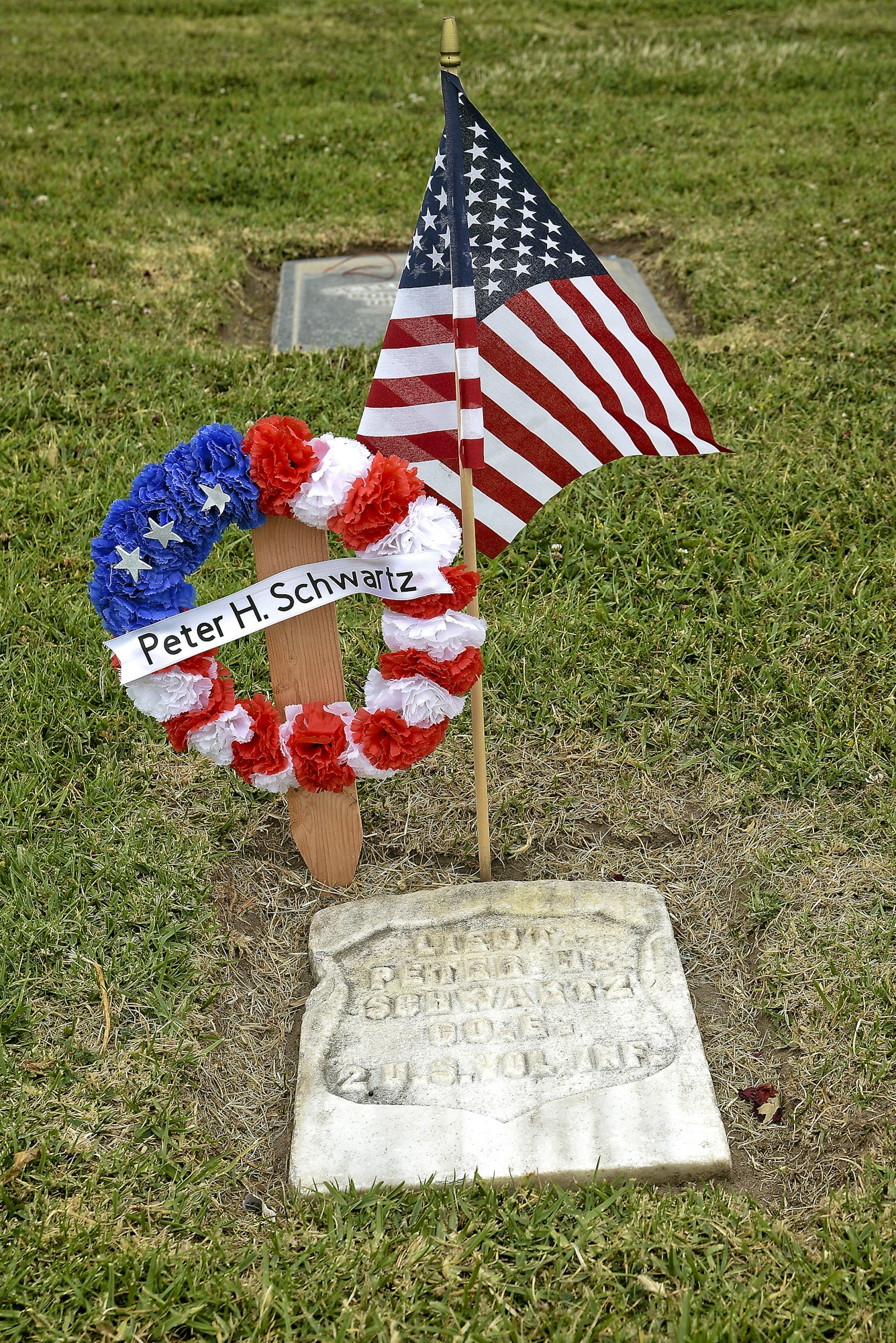 A US flag and a wreath with a name plaque by a weathered gravestone.