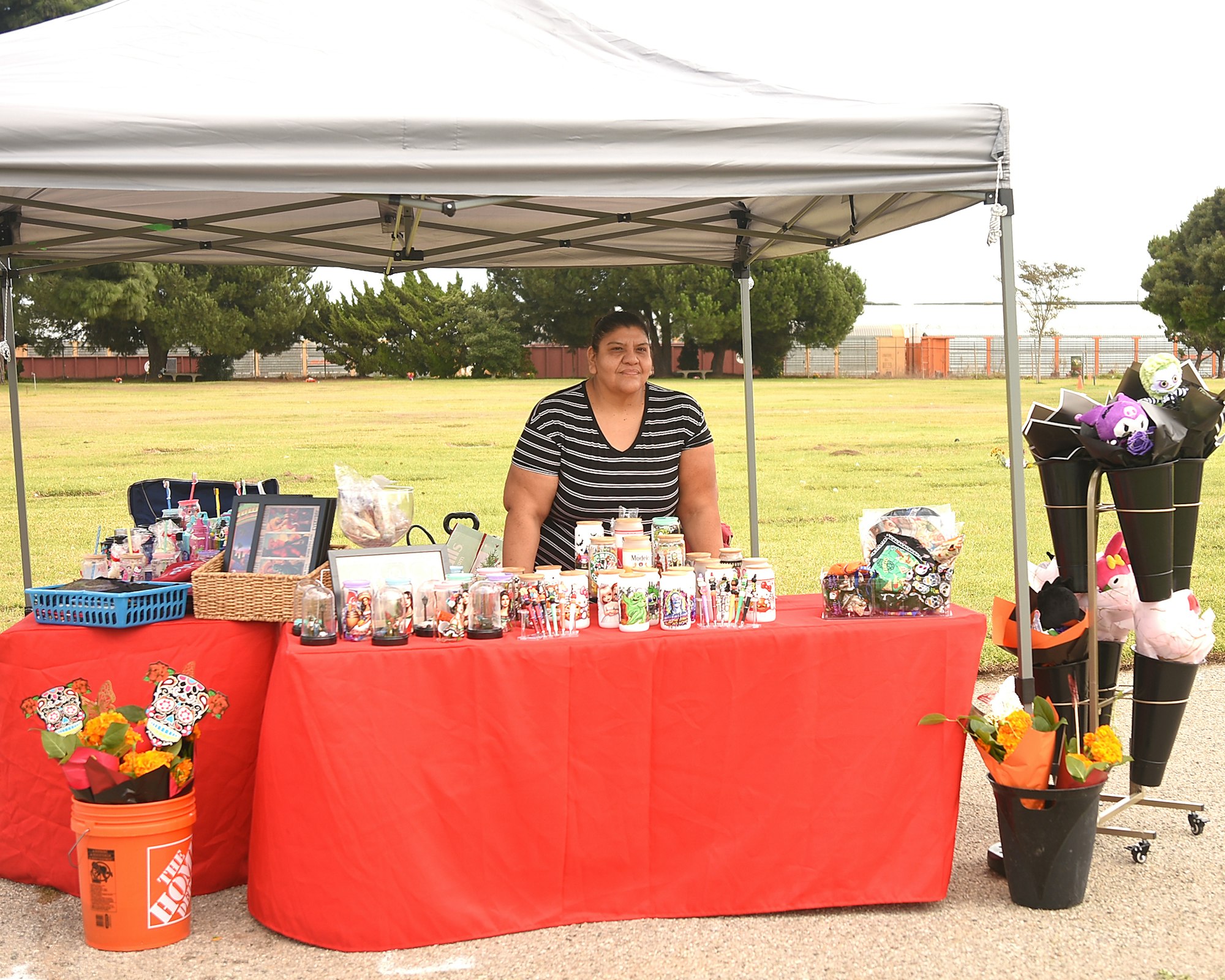 A person at an outdoor stall with various items on display under a canopy.