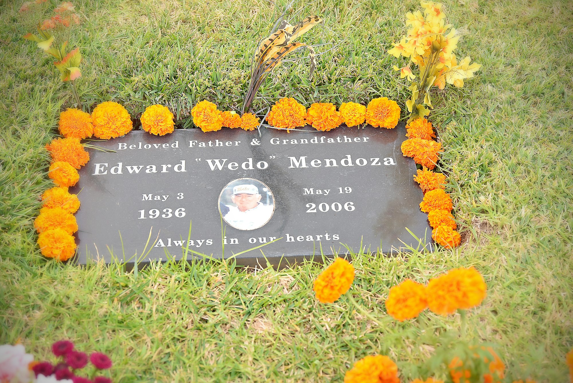 A gravesite with a memorial plaque surrounded by flowers, commemorating a beloved father and grandfather.