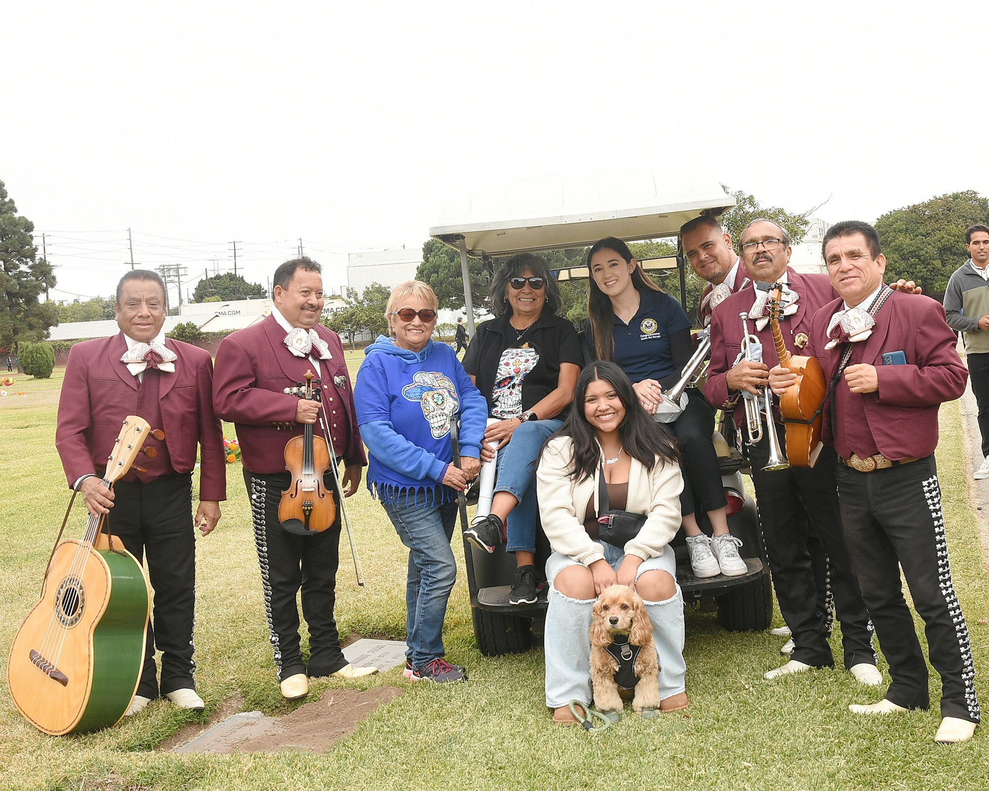 Group of people with a mariachi band, a golf cart, and a dog at an outdoor event.