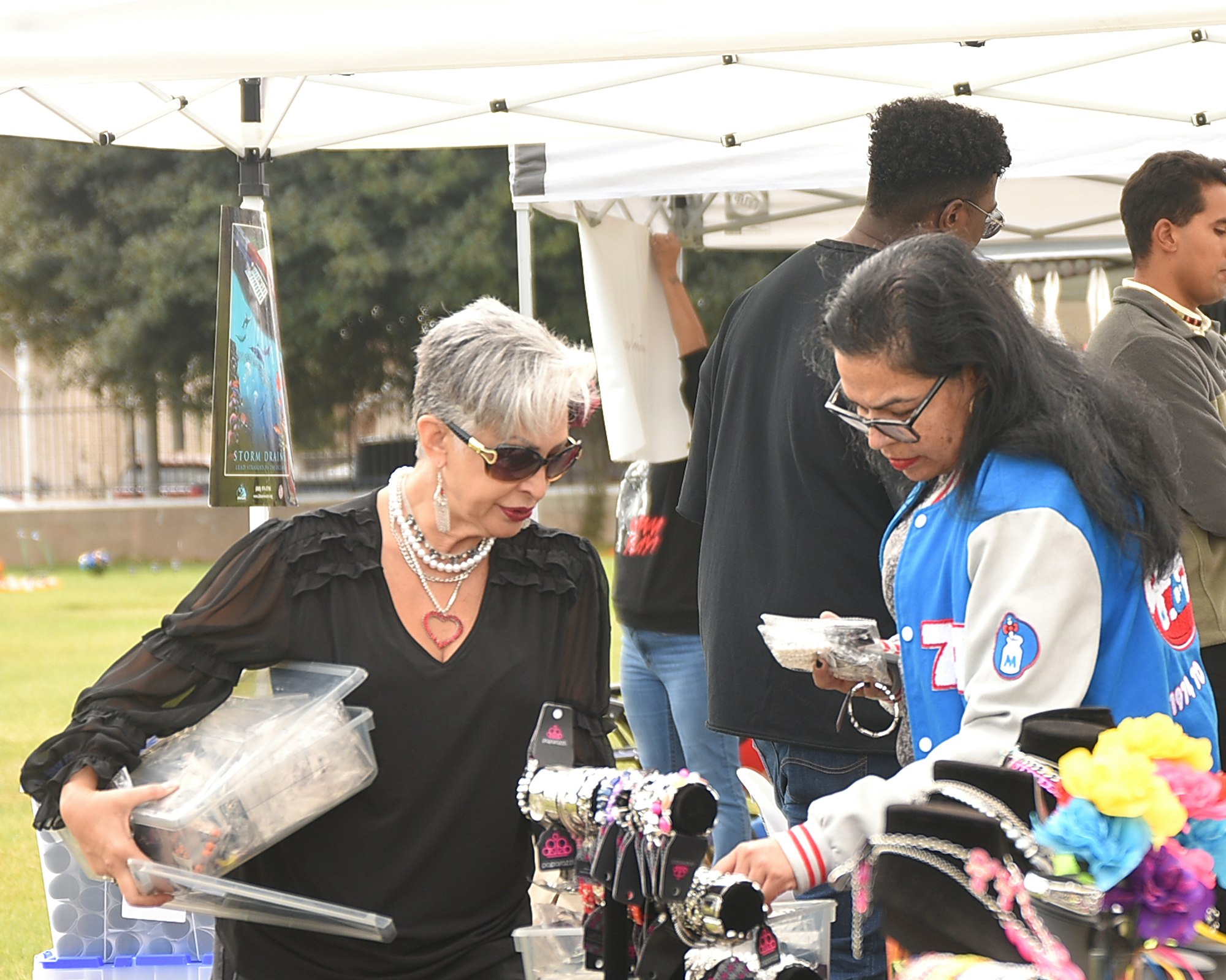 Outdoor market scene with people shopping for accessories and crafts.
