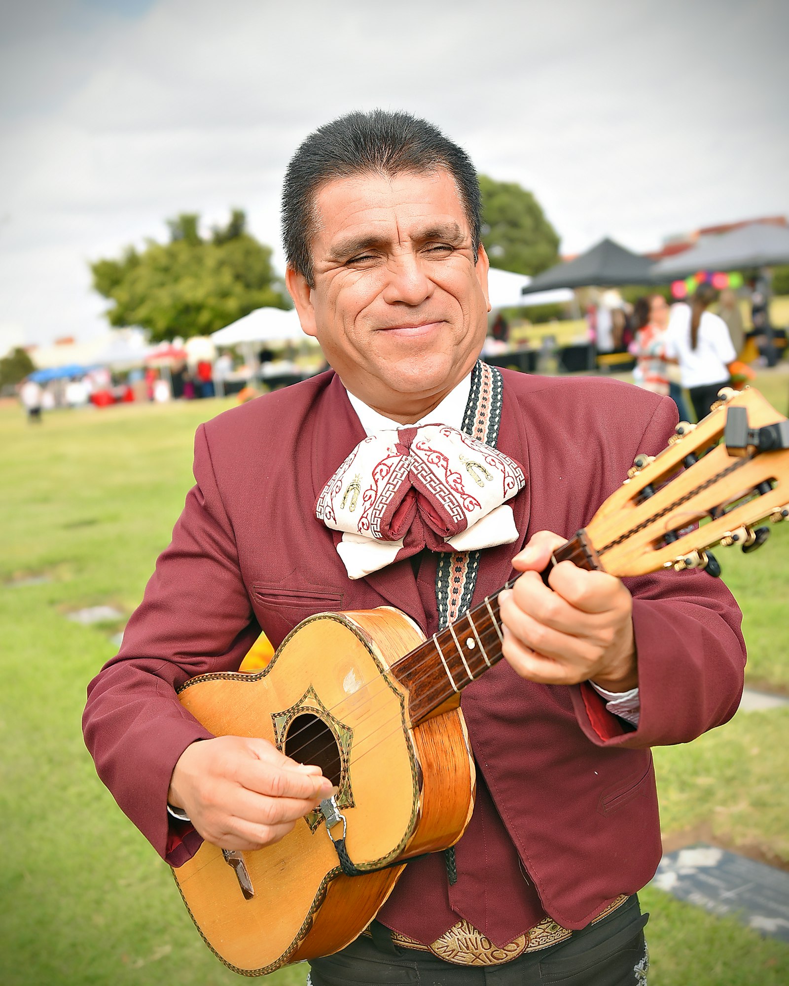 A man playing a small guitar, possibly a mariachi, with a festive background.