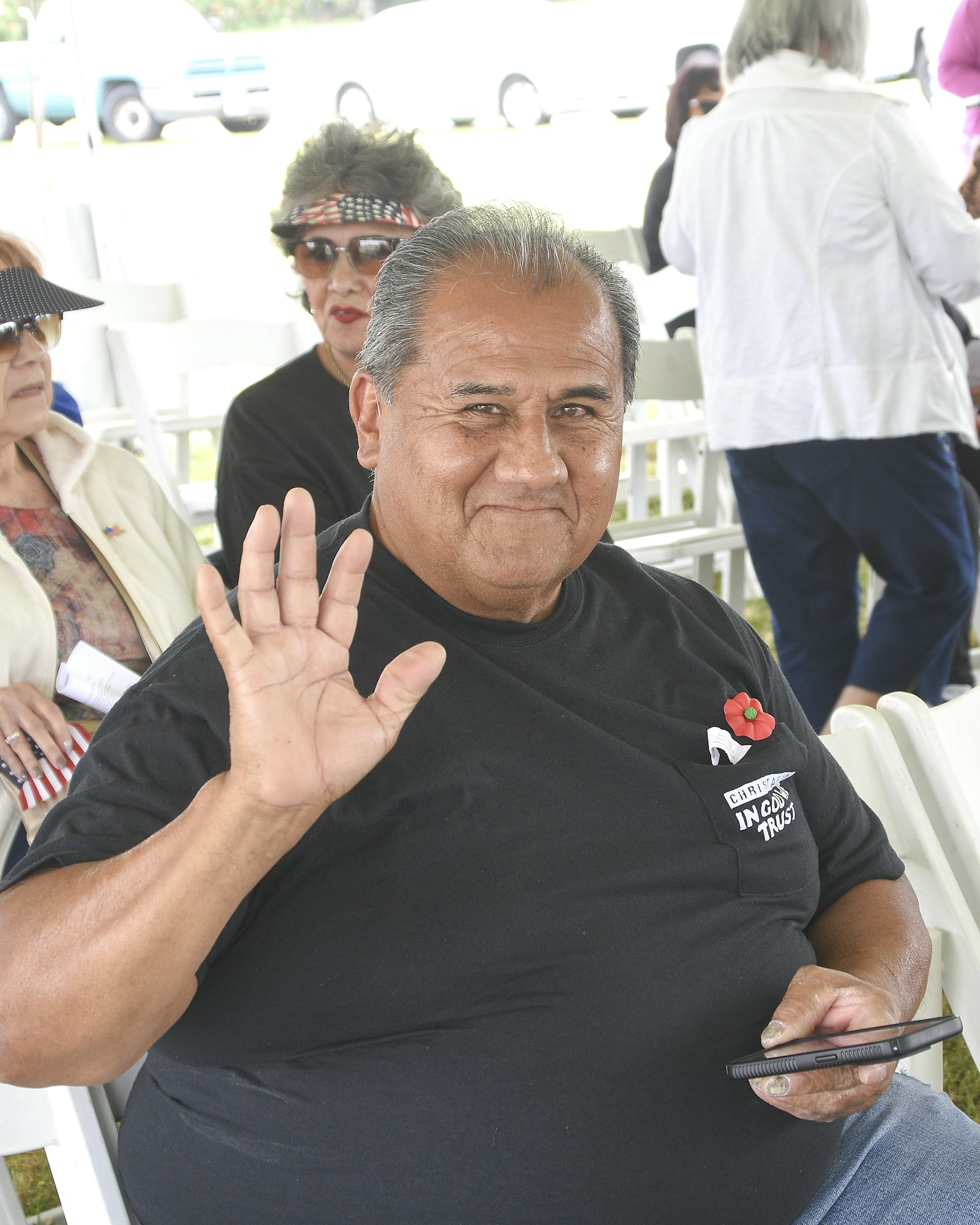 A man waving at the camera with people seated in the background.