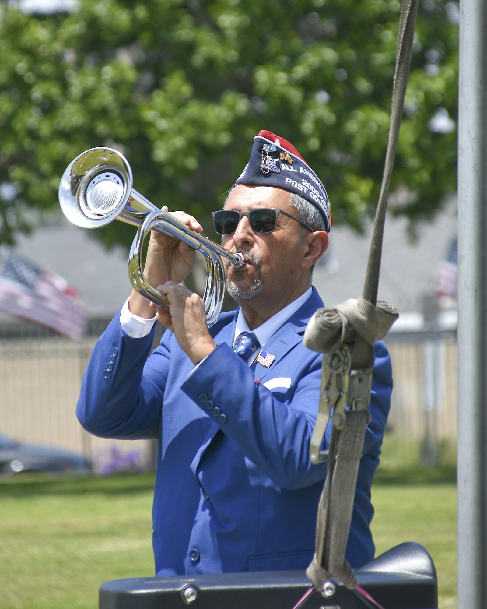 A person in a blue uniform playing a silver bugle, with flags in the background. #music #uniform #ceremony