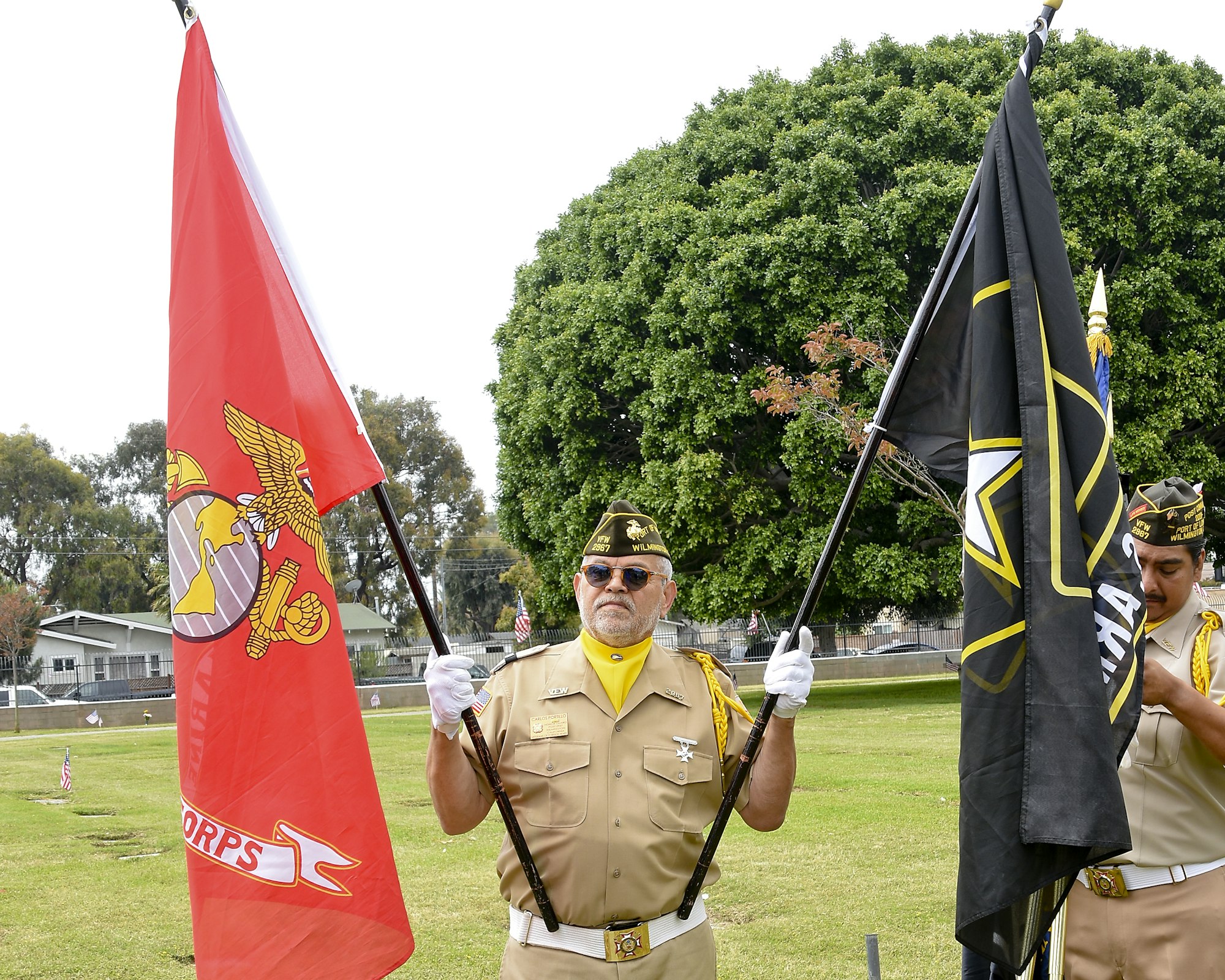 Two people in uniform holding ceremonial flags, standing on grass.