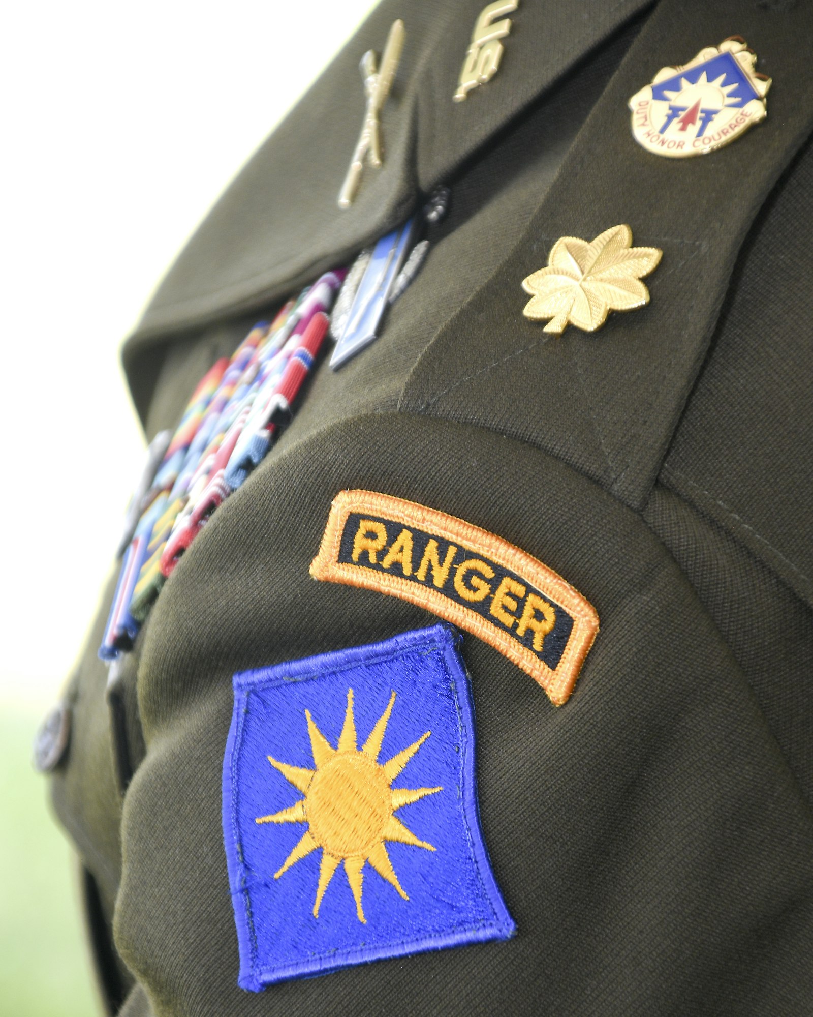 Close-up of a uniform with badges and insignia, including a "RANGER" patch, medals, and a sun emblem.