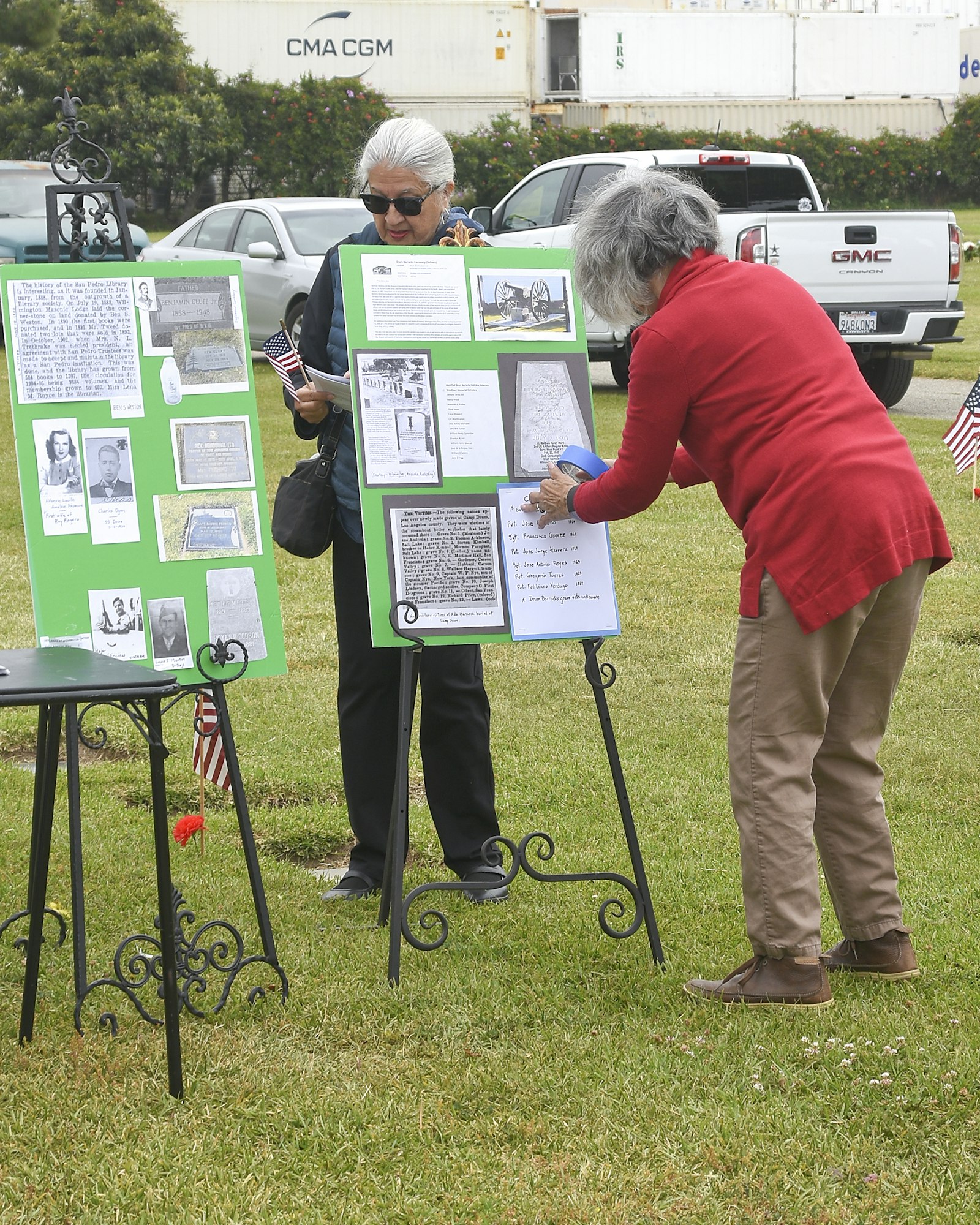 Two people observing a display with information and photos on easels outdoors.
