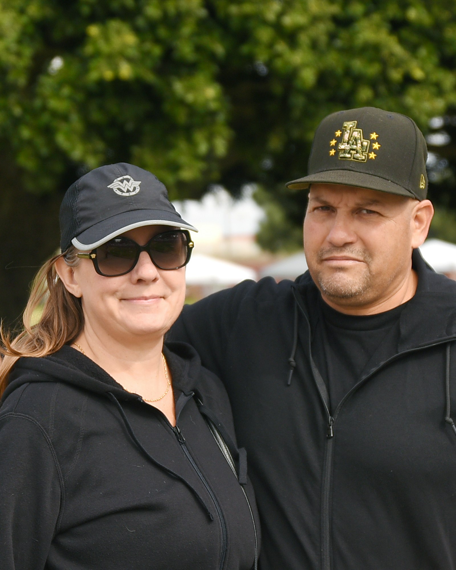 Two people wearing caps and sunglasses outdoors.