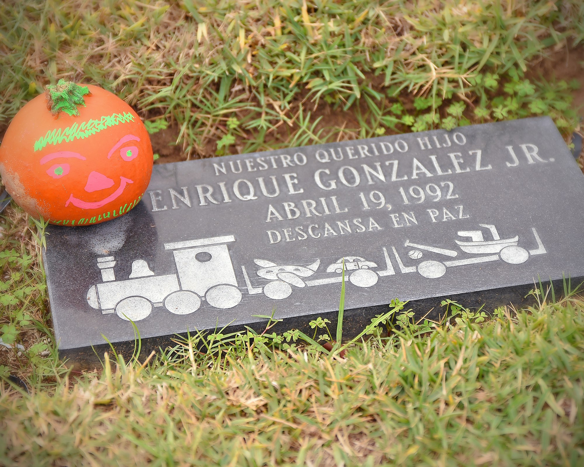 A painted pumpkin on a grave marker with the inscription "Descansa en paz" (Rest in Peace).