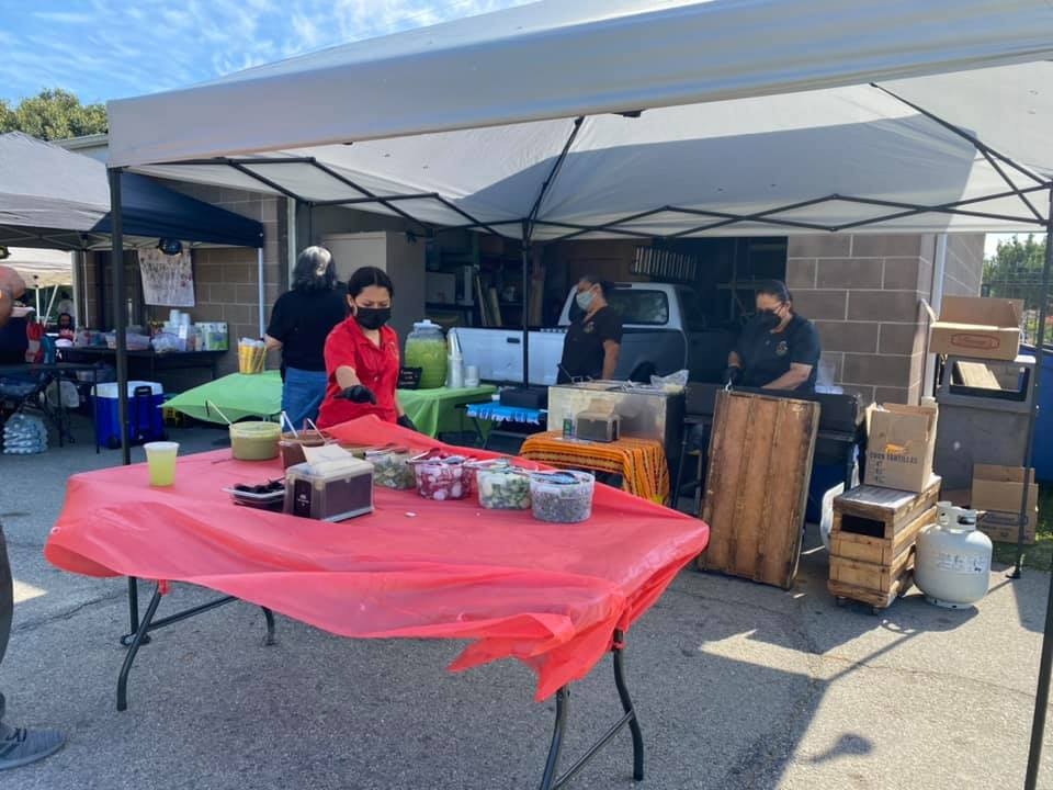A bustling outdoor food market scene with vendors, colorful tables, and various food items on display.