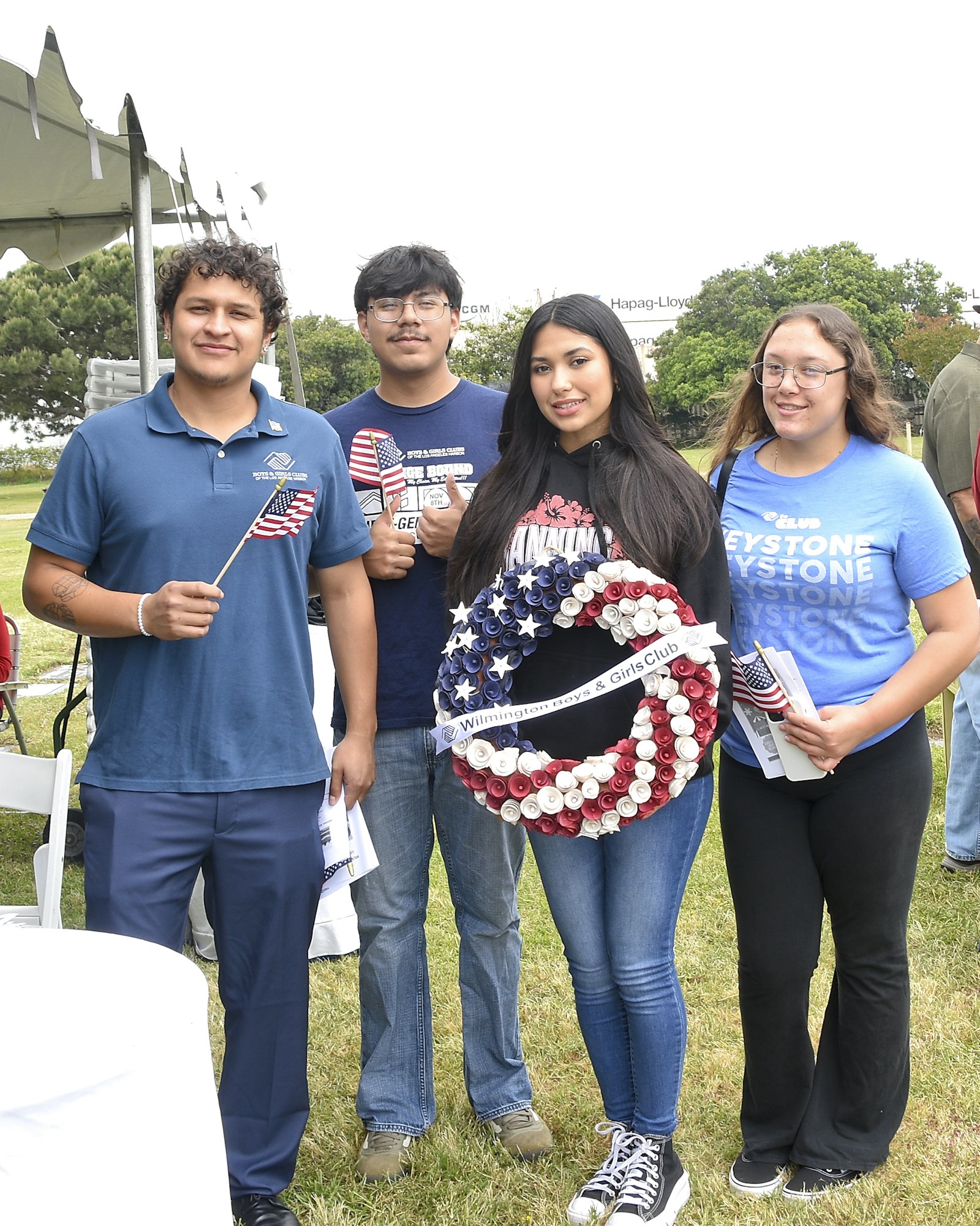 Four individuals holding American flags and a patriotic wreath, possibly at a patriotic or memorial event.