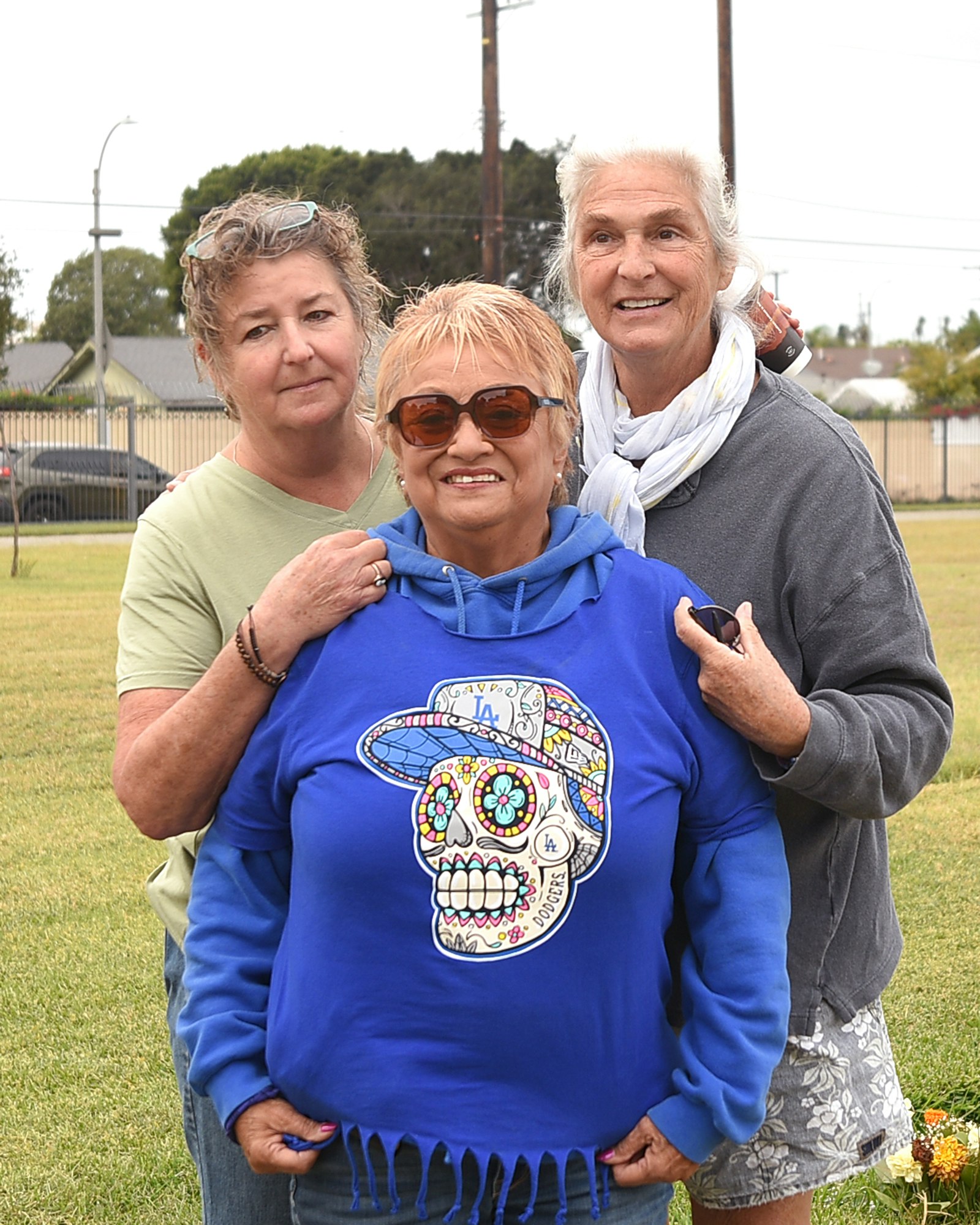 Three people posing together, one wearing a blue hoodie with a colorful skull design, in an outdoor setting.