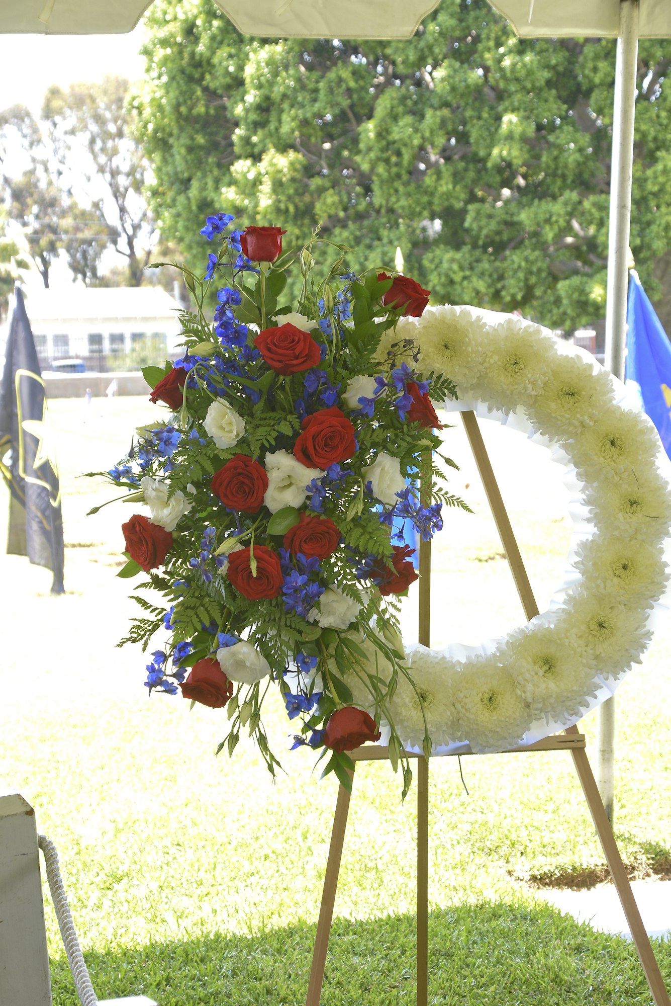 Floral arrangements with red, white, and blue flowers, likely for a commemoration or ceremony, displayed outdoors under a tent.