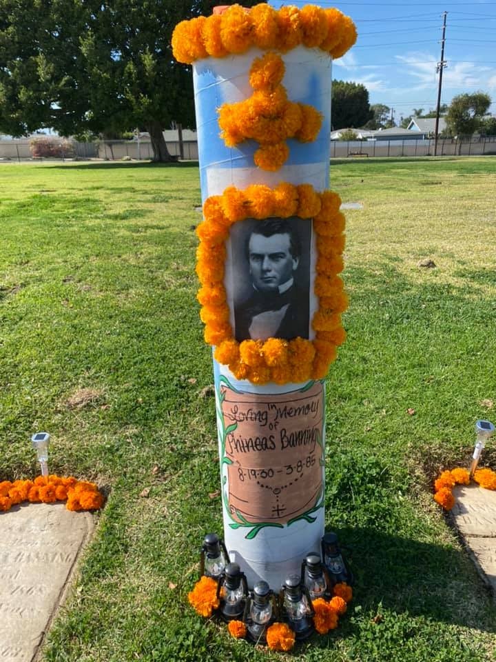 A memorial with a photo of a person named Gineas Banning, adorned with orange flowers and candles, set in a grassy area.
