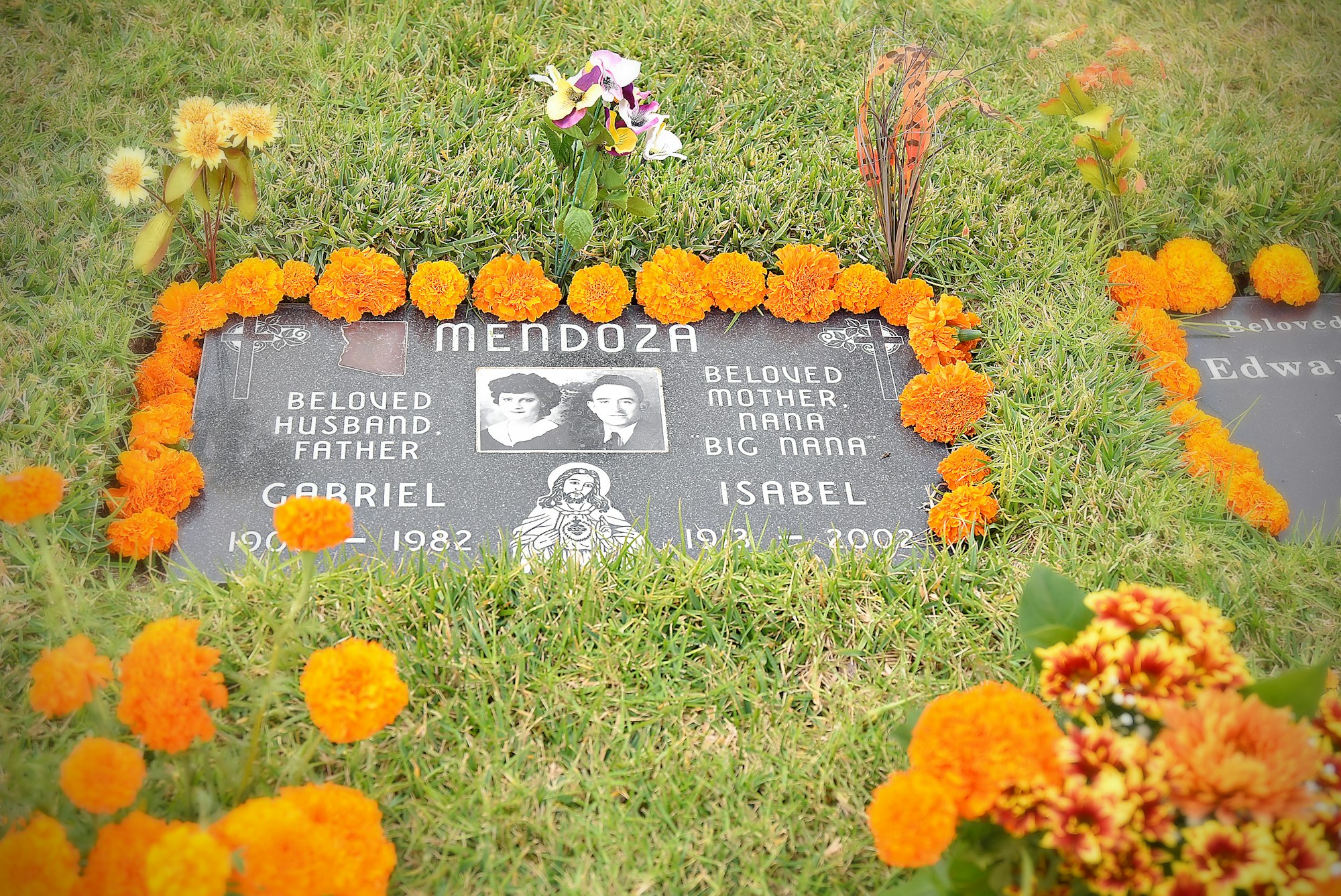 Gravestone with marigold flowers and personal inscriptions, honoring individuals from the Mendoza family.
