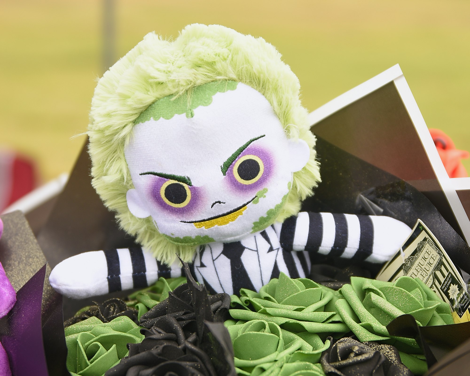 A plush toy resembling a popular comic character, styled in black and white with green hair, displayed atop decorative ribbons.