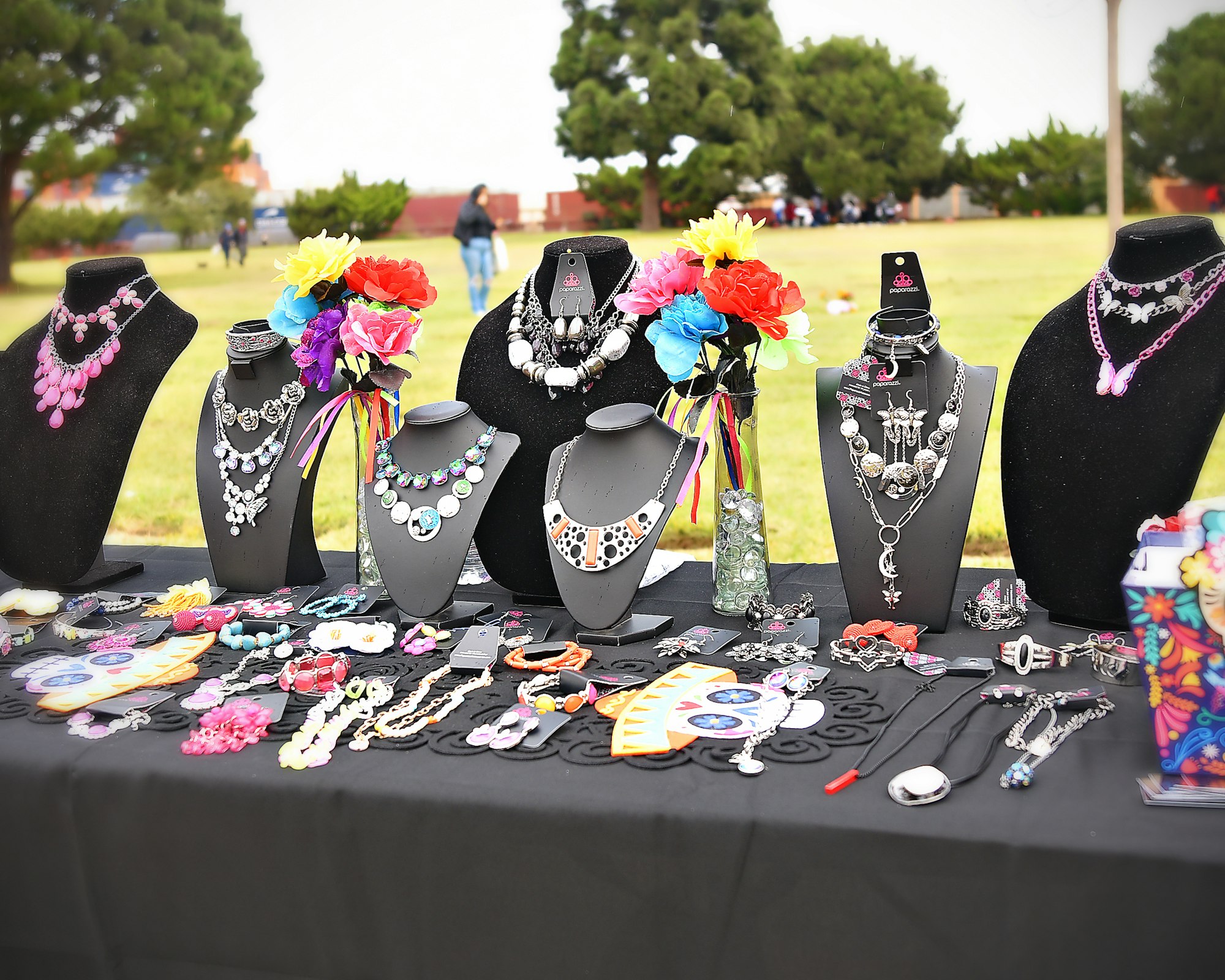 A display of assorted jewelry on mannequin busts and tabletop, with colorful flowers adorning the setup.