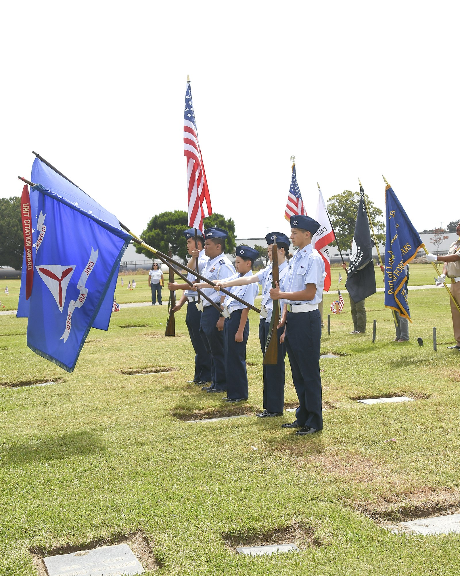 Color guard in uniform holding US flags and military banners on a grassy field.