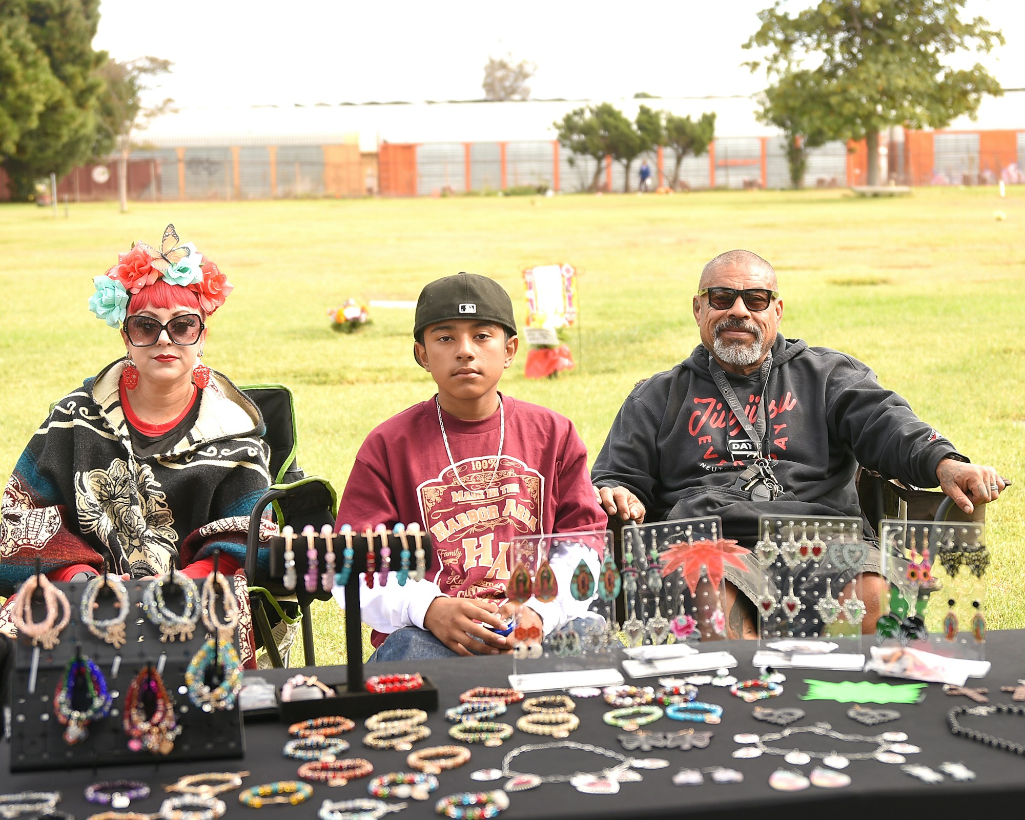 Three people sitting behind a display of colorful jewelry at an outdoor market.