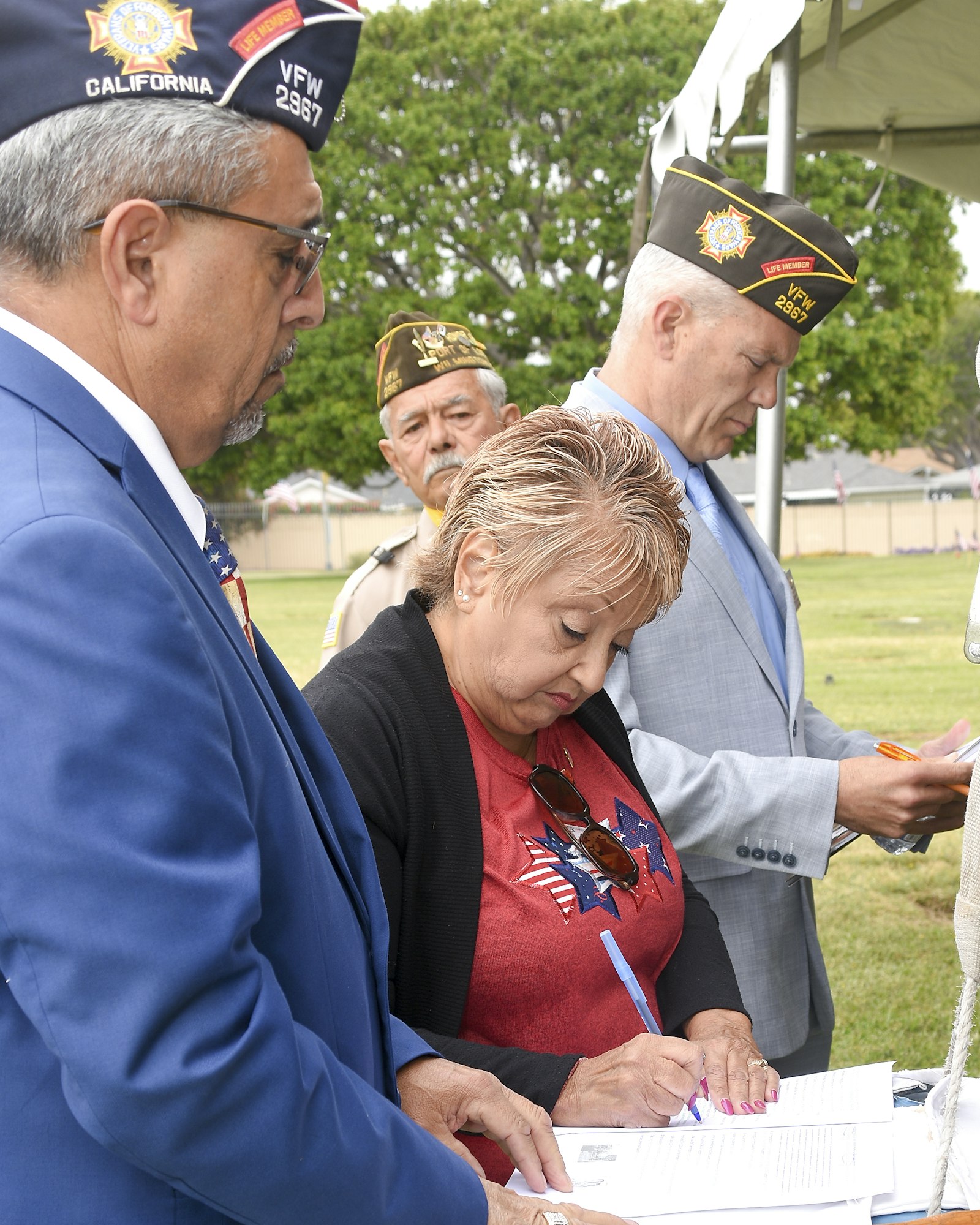 People in ceremonial attire signing documents outdoors.