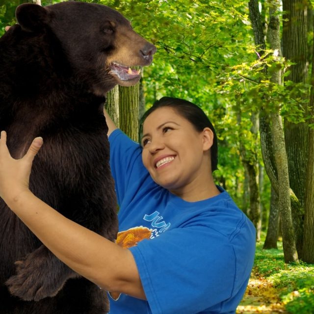 A person smiling and hugging a bear in a forest setting.
