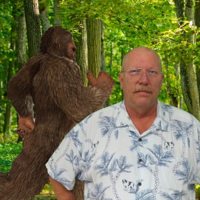 A man in a patterned shirt stands in a forest with a creature resembling Bigfoot in the background.