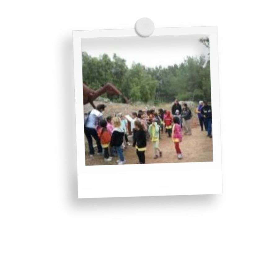 A group of children outdoors near a statue or structure, with trees in the background.