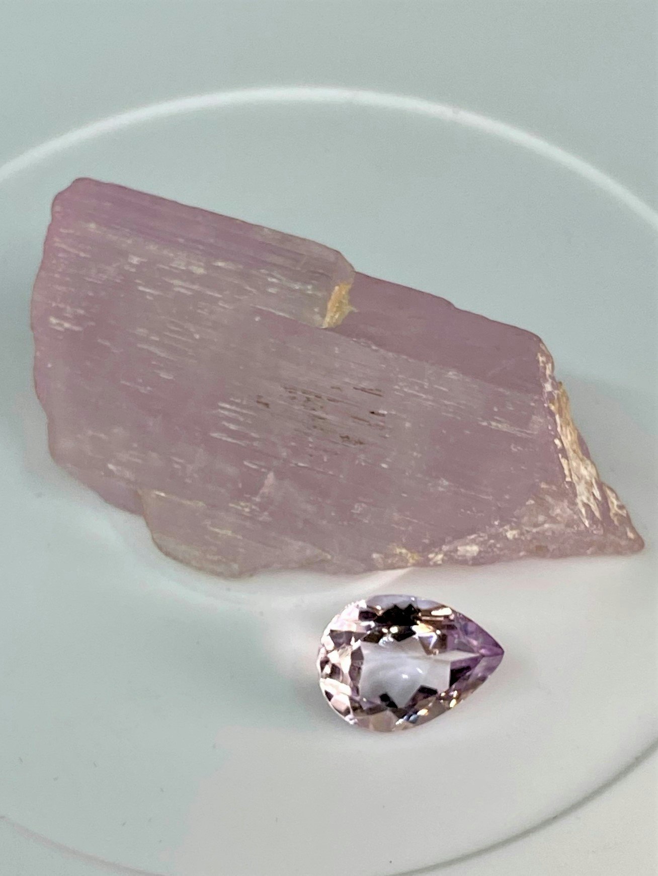 A raw pink crystal and a faceted gemstone on a white surface.