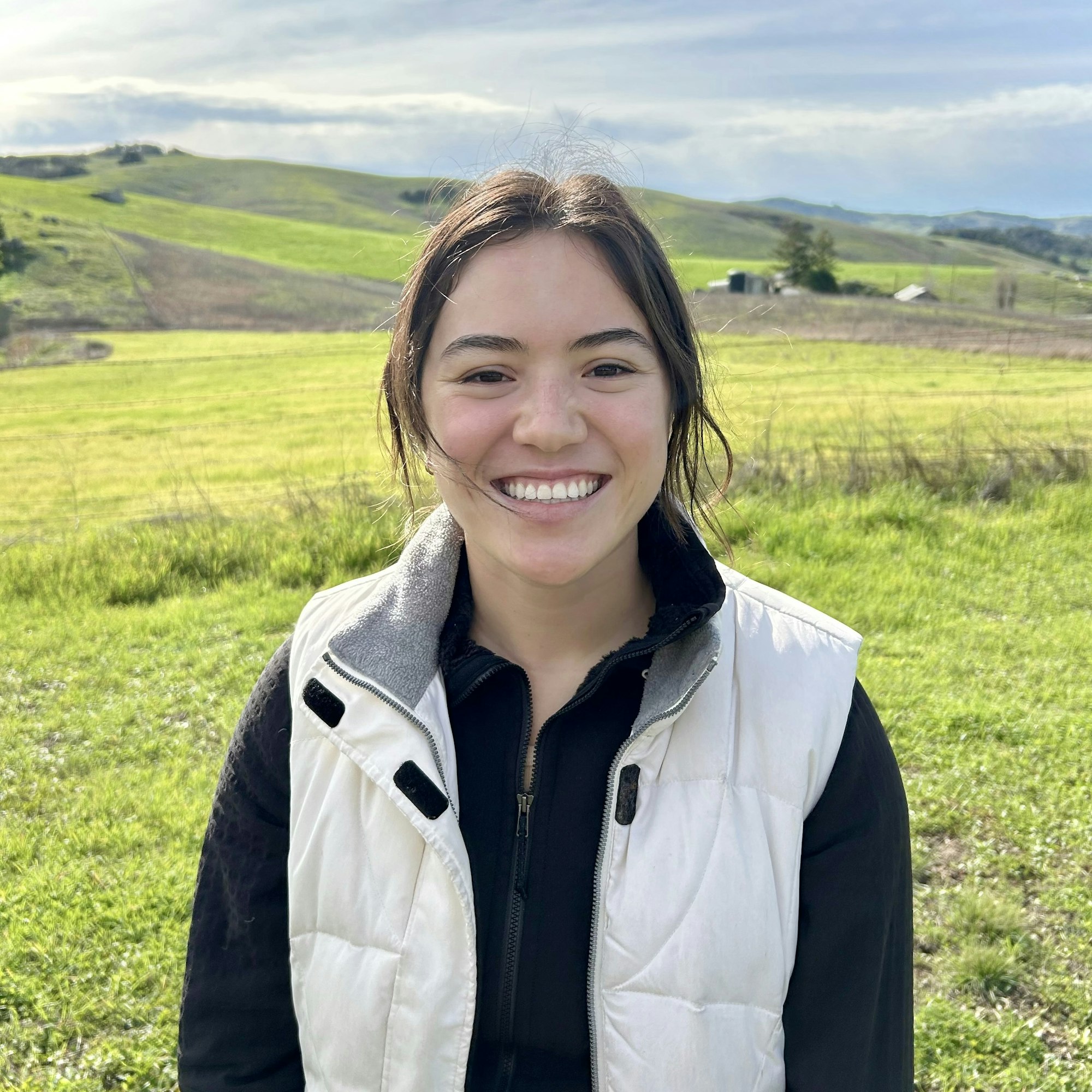 A smiling person with a rural landscape in the background.