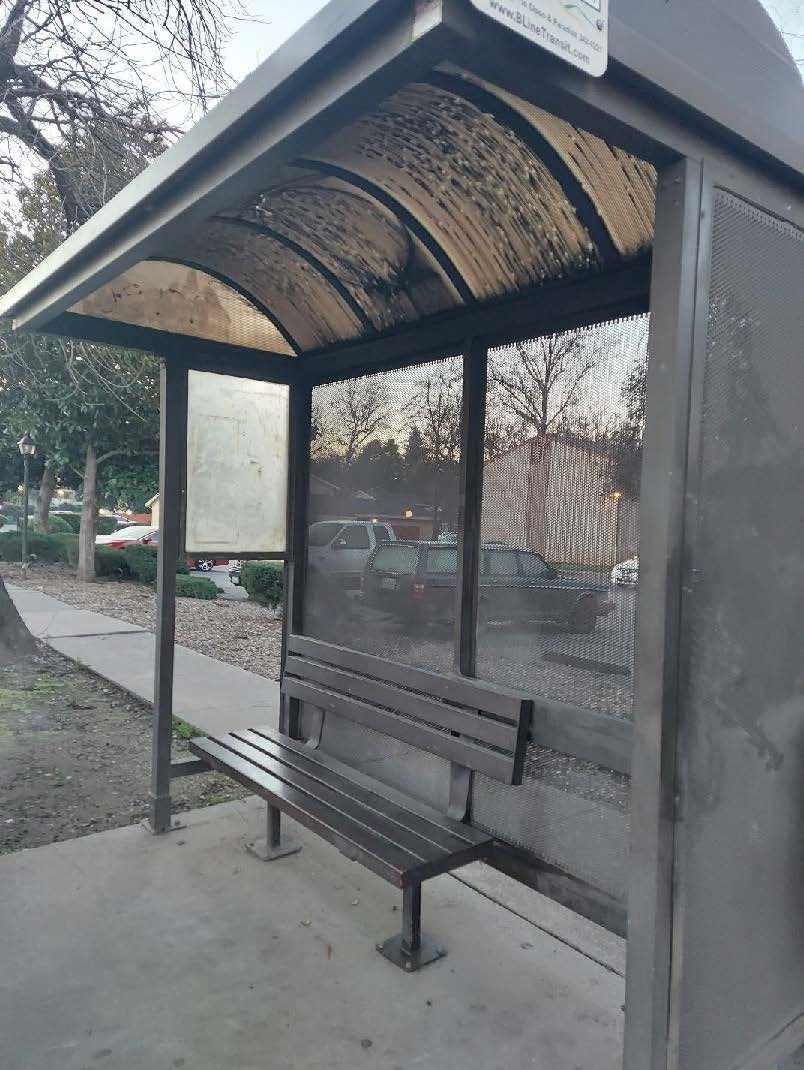A bus stop shelter with a bench and a canopy, located next to a sidewalk.