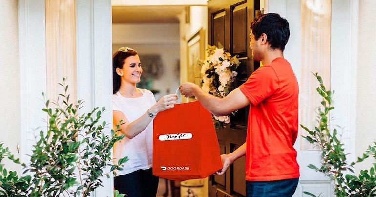 A delivery person hands a DoorDash bag to a woman standing at her door.