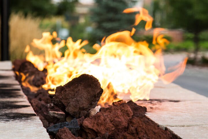 A fire feature with flames rising over decorative rocks, set outdoors.