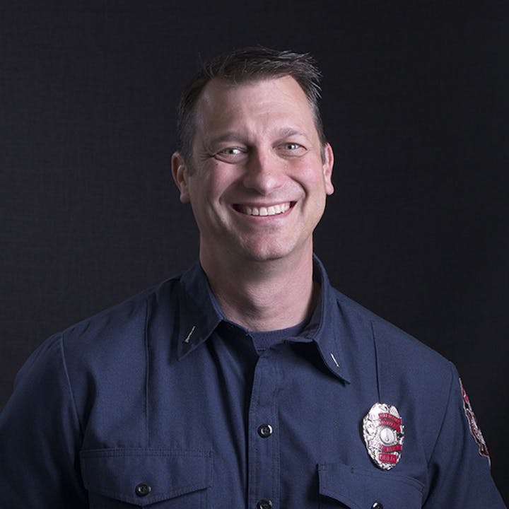 A smiling man in a blue uniform with a badge on the chest.