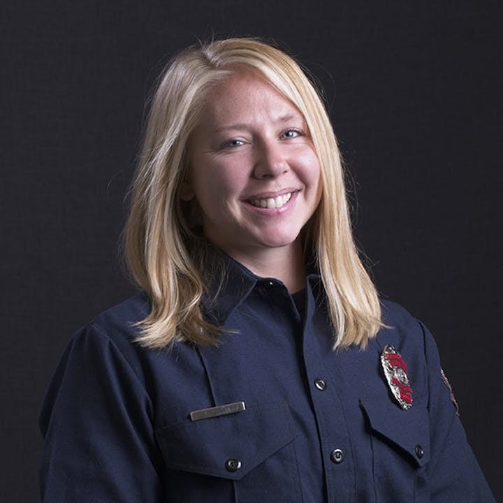 A person in a firefighter uniform smiling against a dark background.