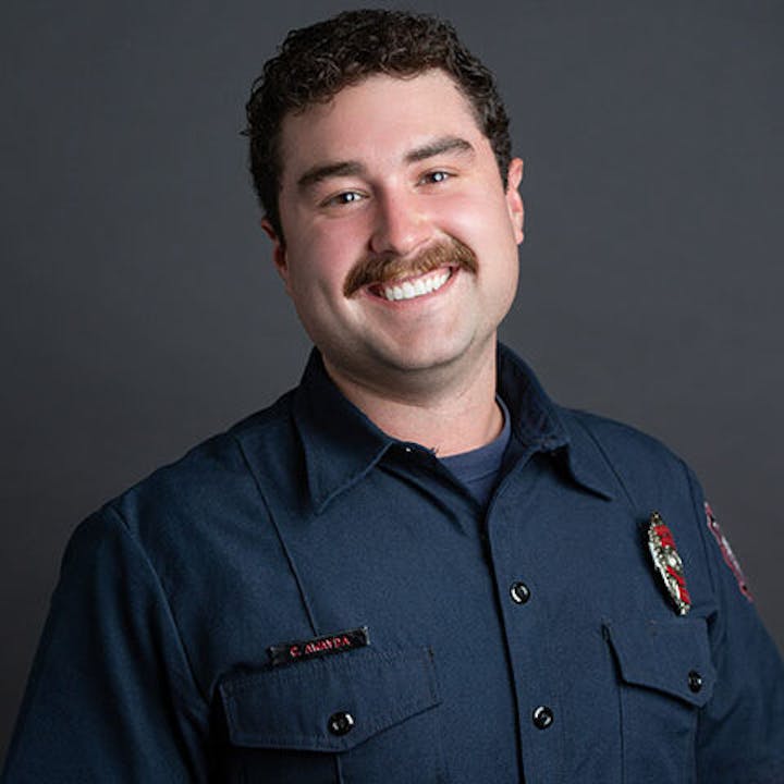 A person in a navy-blue uniform, smiling against a gray background.