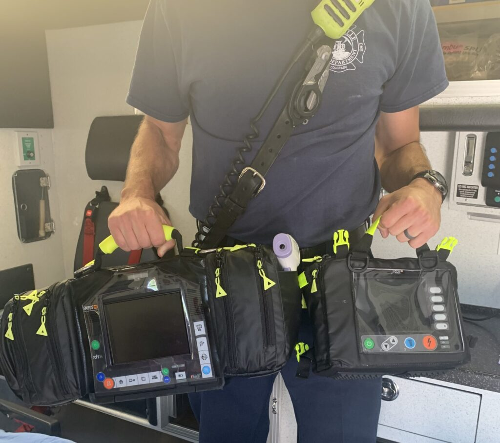 Person holding emergency medical gear inside a vehicle, with a portable monitor visible.