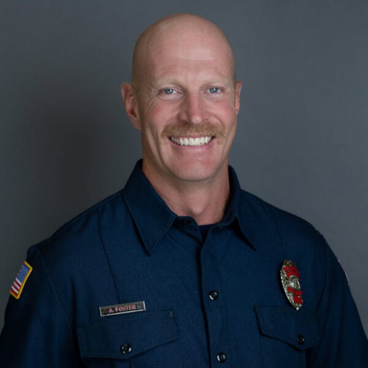 A smiling person wearing a dark uniform with a badge and an American flag patch.