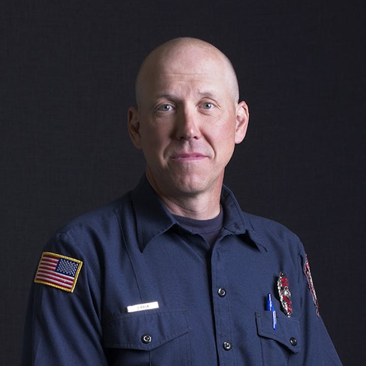 A person in a uniform with shirt badge, pen, and USA flag on the sleeve.