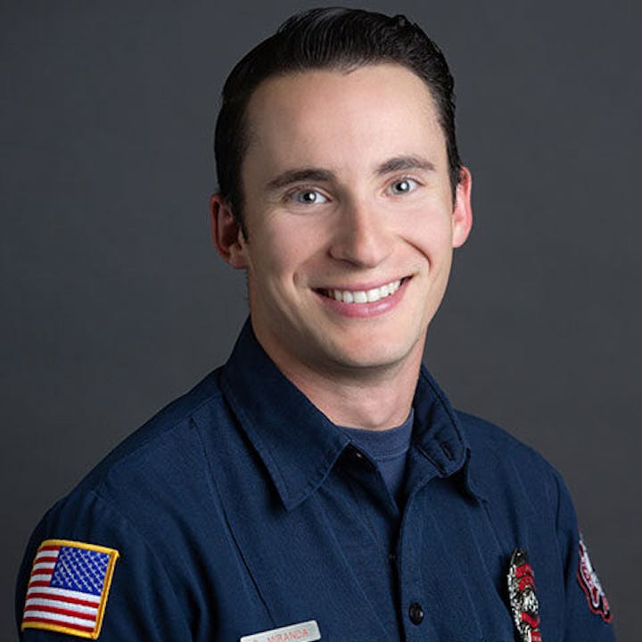 A person in a dark uniform with an American flag patch and a badge, smiling at the camera.
