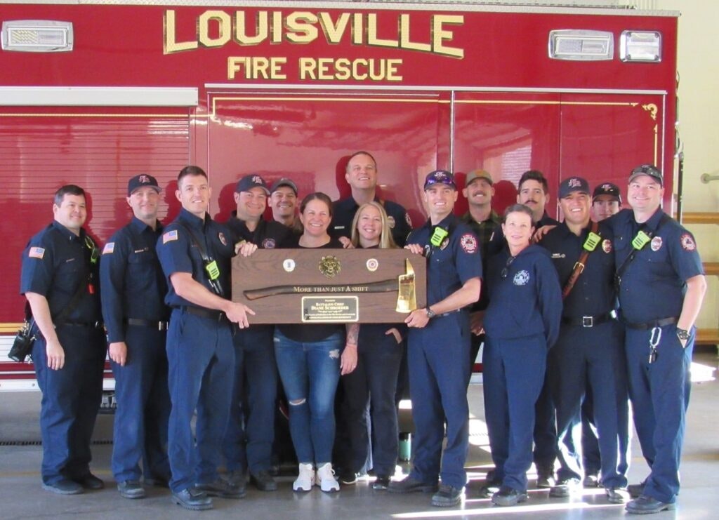 A group of firefighters posing with a plaque in front of a fire rescue vehicle.