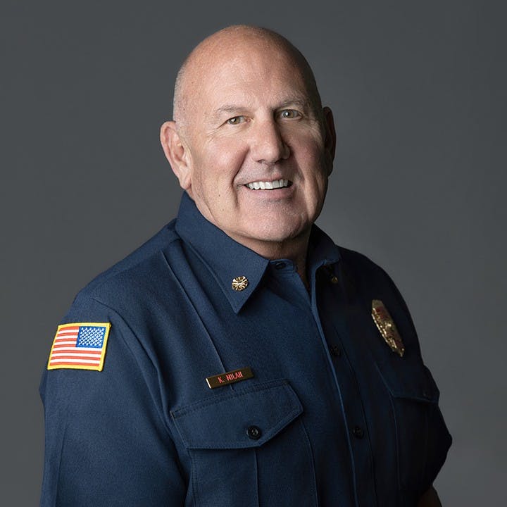 A smiling man in a blue uniform with an American flag patch, likely a firefighter or similar public service role.