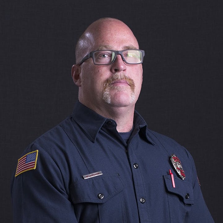 A person wearing a blue uniform with an American flag patch and a badge.