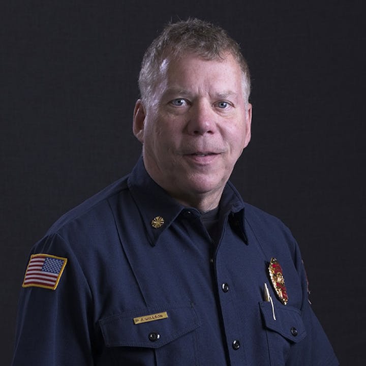 A person in a firefighter uniform with badges and a U.S. flag patch on the sleeve.