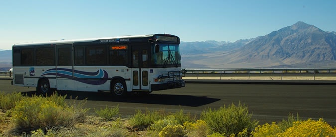 A bus on a road with mountains in the background.